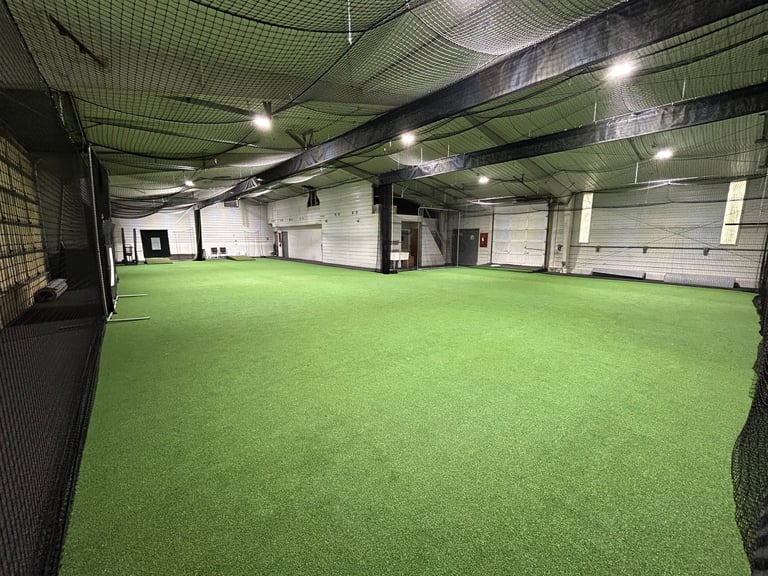 Large indoor soccer or sports facility with bright green artificial turf field and industrial ceiling with lights