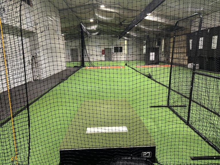 Interior of indoor baseball batting cage with bright green turf floor and black netting surrounding the field